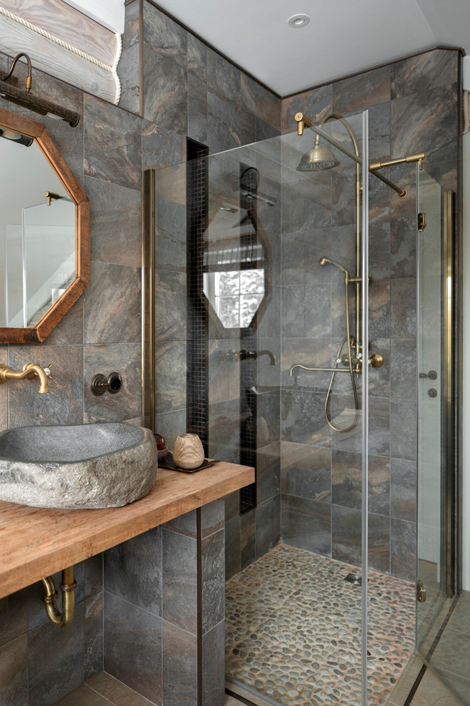 Cette image montre une salle d'eau chalet de taille moyenne avec une douche d'angle, un carrelage gris, des carreaux de porcelaine, un sol en carrelage de porcelaine, une vasque, un plan de toilette en bois, un sol beige, une cabine de douche à porte battante et un plan de toilette marron.