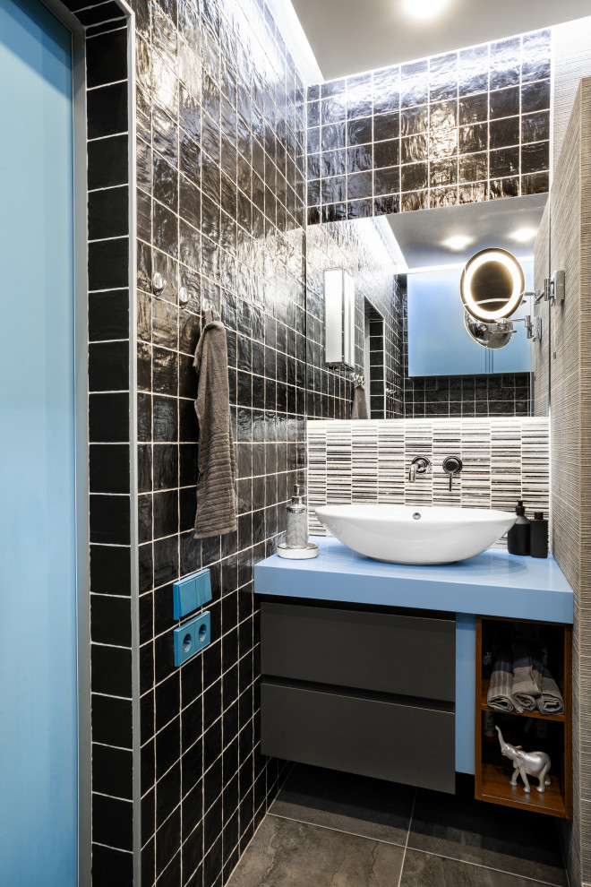 Modernes Badezimmer mit flächenbündigen Schrankfronten, schwarzen Schränken, schwarzen Fliesen, Aufsatzwaschbecken, grauem Boden und blauer Waschtischplatte in Sonstige