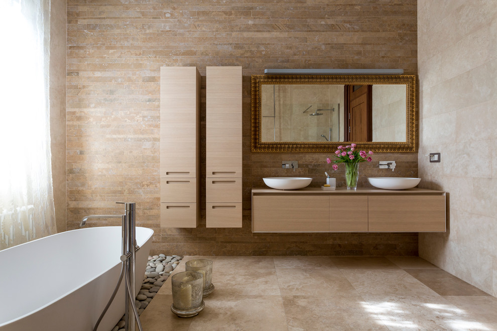 Réalisation d'une salle de bain design en bois clair avec un placard à porte plane, une baignoire indépendante, un carrelage beige, un mur beige et une vasque.