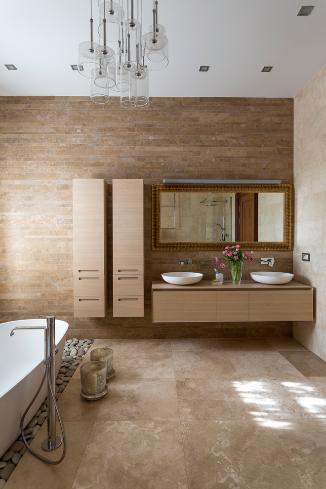 Foto de cuarto de baño actual con lavabo sobreencimera, armarios con paneles lisos, puertas de armario de madera clara, bañera exenta y baldosas y/o azulejos marrones