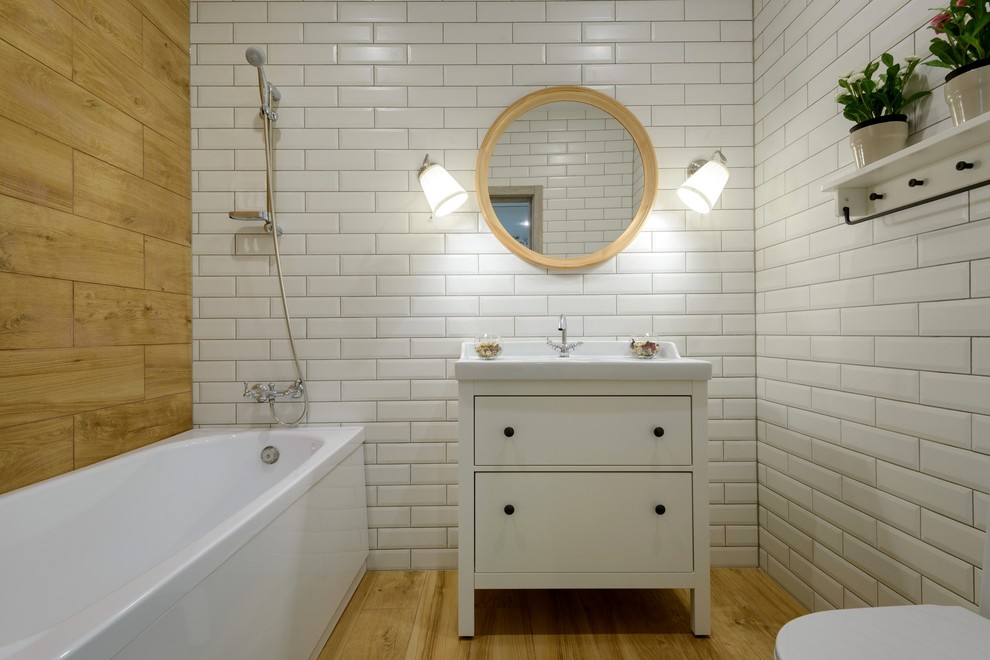 Пример оригинального дизайна: ванная комната в белых тонах с отделкой деревом в скандинавском стиле с плоскими фасадами, белыми фасадами, накладной ванной, душем над ванной, белой плиткой, плиткой кабанчик, паркетным полом среднего тона и монолитной раковиной