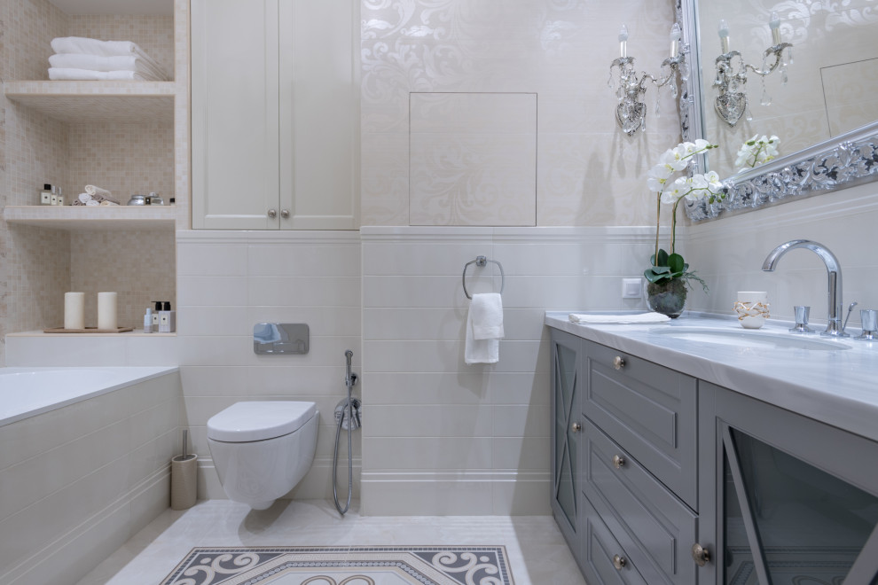 На фото: главная ванная комната в современном стиле с серыми фасадами, ванной в нише, душем над ванной, инсталляцией, бежевой плиткой, белой плиткой, врезной раковиной и разноцветным полом
