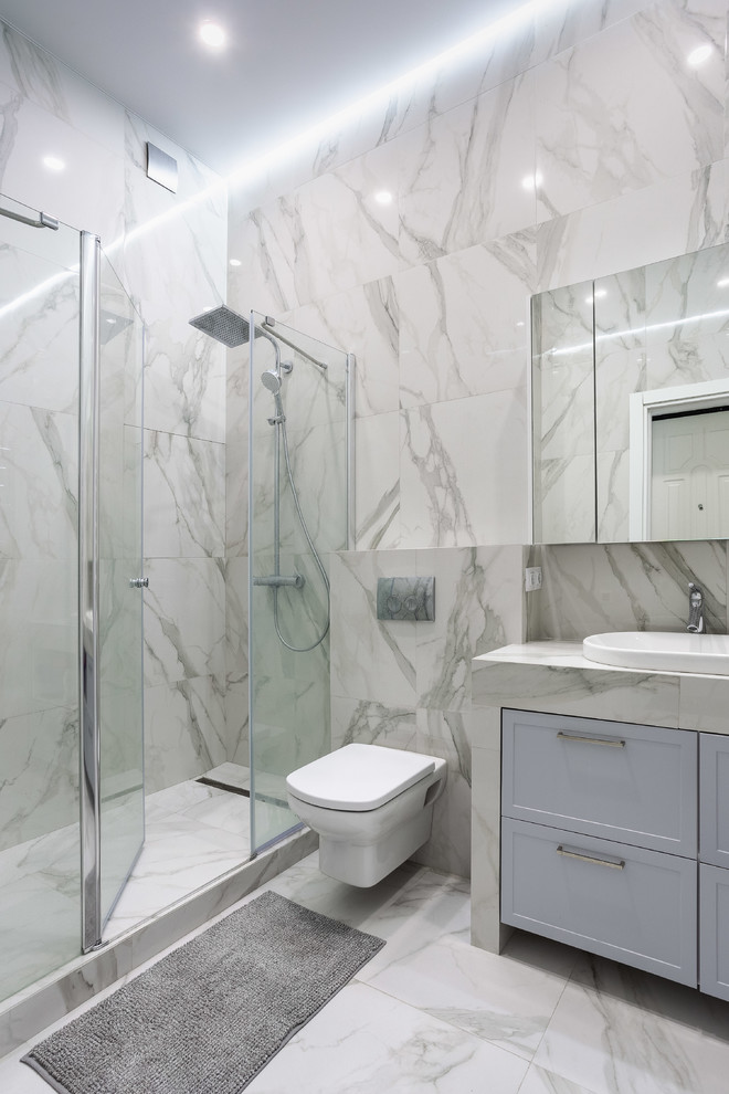 Bild på ett vintage grå grått badrum, med luckor med infälld panel, blå skåp, en dusch i en alkov, en vägghängd toalettstol, grå kakel, grå väggar, ett nedsänkt handfat, grått golv och dusch med gångjärnsdörr