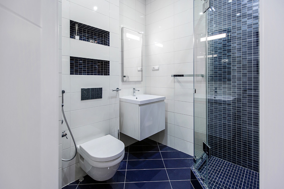 На фото: ванная комната в скандинавском стиле с плоскими фасадами, белыми фасадами, угловым душем, инсталляцией, синей плиткой, белой плиткой, плиткой мозаикой, белыми стенами, душевой кабиной, подвесной раковиной и душем с распашными дверями с