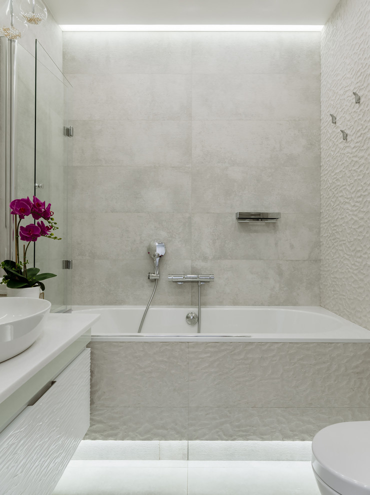 На фото: главная ванная комната среднего размера в современном стиле с плоскими фасадами, белыми фасадами, ванной в нише, душем над ванной, инсталляцией, бежевой плиткой, керамогранитной плиткой, бежевыми стенами, полом из керамогранита, накладной раковиной, столешницей из искусственного кварца, бежевым полом, шторкой для ванной и белой столешницей с