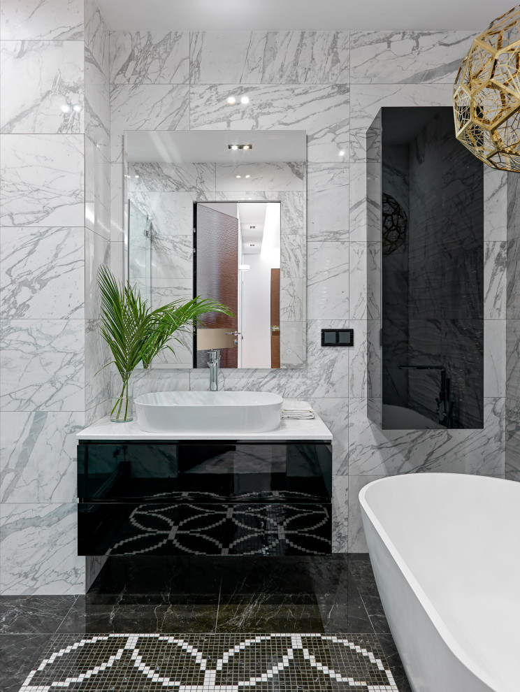 Идея дизайна: ванная комната среднего размера в современном стиле с плоскими фасадами, черными фасадами, отдельно стоящей ванной, душевой комнатой, инсталляцией, белой плиткой, керамогранитной плиткой, белыми стенами, полом из мозаичной плитки, душевой кабиной, накладной раковиной, столешницей из искусственного камня, черным полом, душем с распашными дверями и белой столешницей