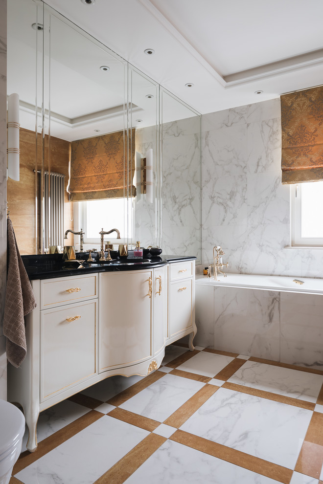 Пример оригинального дизайна: главная ванная комната в классическом стиле с бежевыми фасадами, белой плиткой, разноцветным полом, черной столешницей, фасадами с утопленной филенкой, ванной в нише и зеркалом с подсветкой
