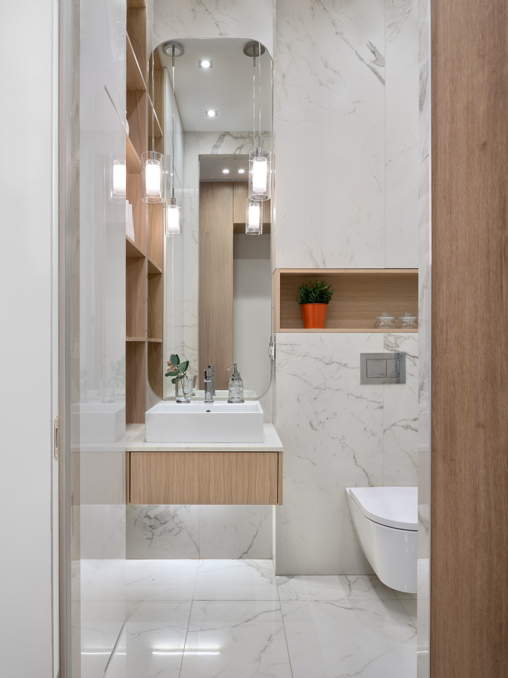 Imagen de cuarto de baño flotante contemporáneo pequeño con armarios con paneles lisos, puertas de armario de madera clara, sanitario de pared, lavabo sobreencimera, suelo blanco, encimeras blancas y aseo y ducha
