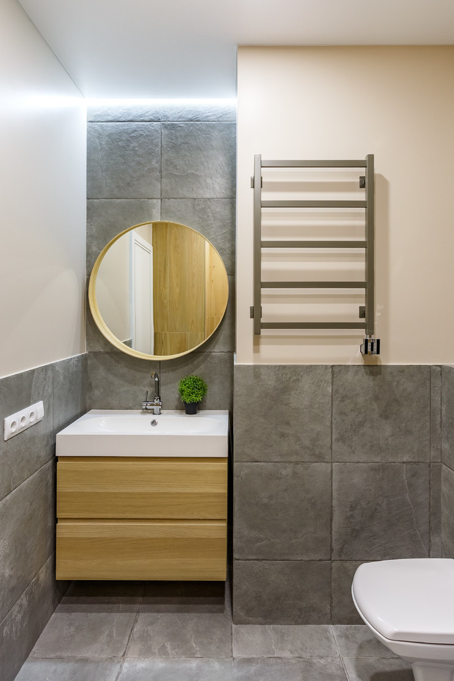 Idées déco pour une salle de bain contemporaine en bois clair avec un placard à porte plane, un carrelage gris, un mur beige, un lavabo intégré et un sol gris.
