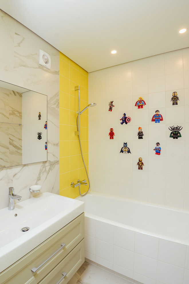 На фото: ванная комната среднего размера в современном стиле с фасадами в стиле шейкер, желтыми фасадами, ванной в нише, душем над ванной, желтой плиткой, керамогранитной плиткой, полом из керамогранита, монолитной раковиной, серым полом, открытым душем и белой столешницей