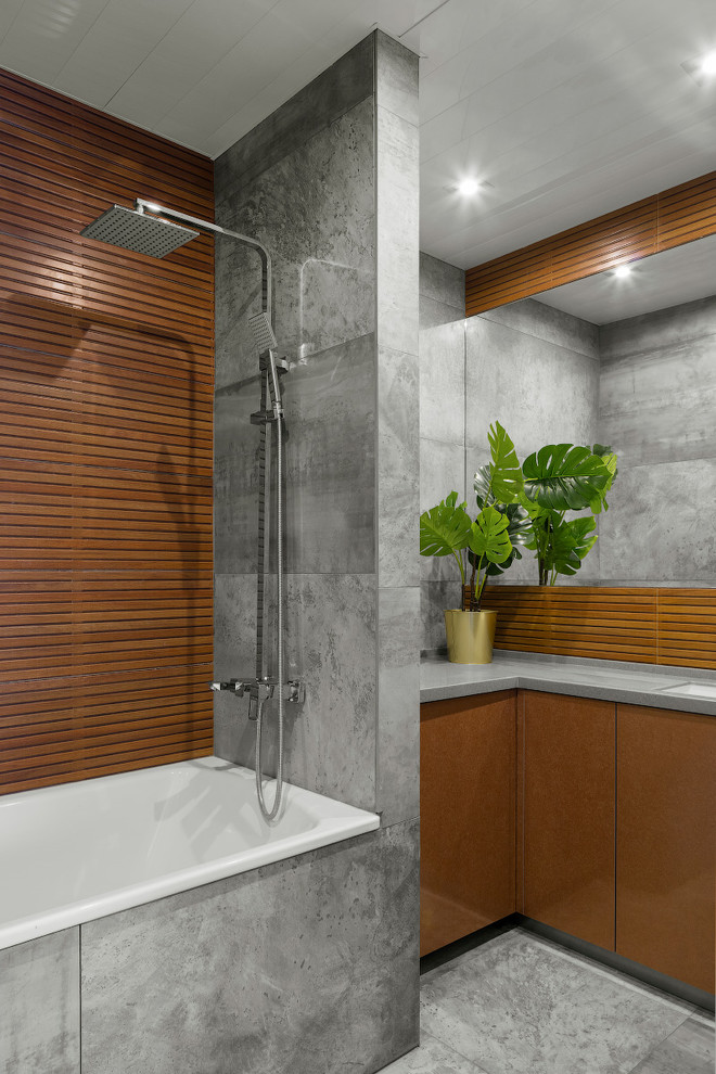 Cette image montre une salle de bain principale design avec un placard à porte plane, des portes de placard marrons, une baignoire en alcôve, un carrelage gris, un lavabo encastré, un sol gris et un plan de toilette gris.