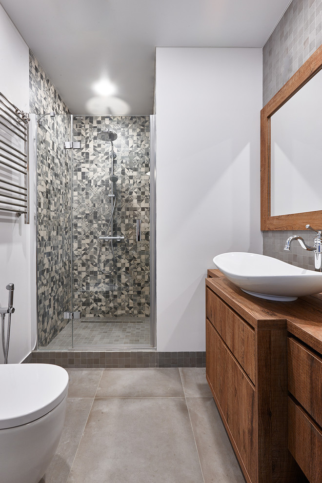 Inredning av ett modernt brun brunt badrum med dusch, med släta luckor, skåp i mellenmörkt trä, en dusch i en alkov, grå kakel, vita väggar, ett fristående handfat, träbänkskiva, grått golv och dusch med gångjärnsdörr