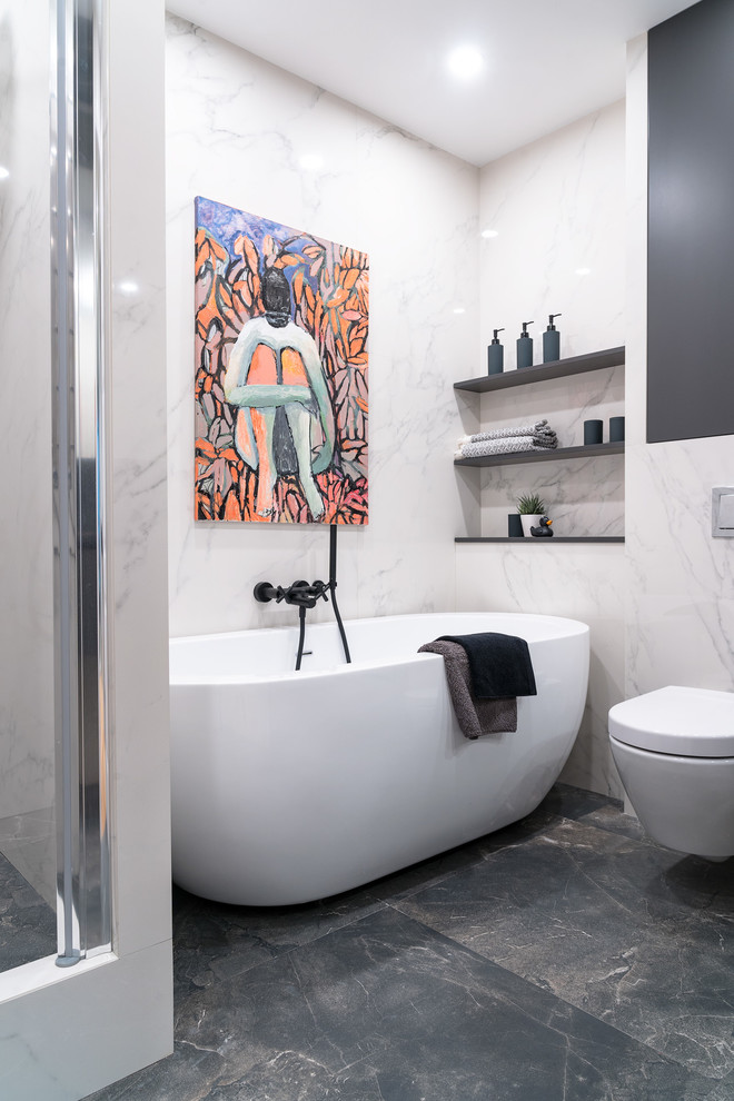 Modelo de cuarto de baño actual con bañera exenta, sanitario de pared, baldosas y/o azulejos blancos y suelo gris