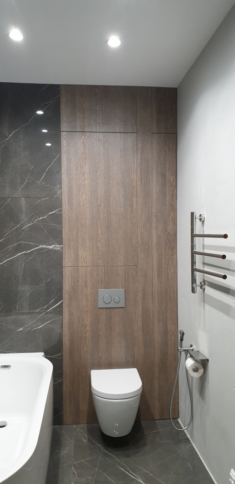 This is an example of a small ensuite bathroom in Moscow with flat-panel cabinets, brown cabinets, a freestanding bath, a wall mounted toilet, black and white tiles, porcelain tiles, grey walls, porcelain flooring, a pedestal sink, grey floors, an enclosed toilet and wood walls.