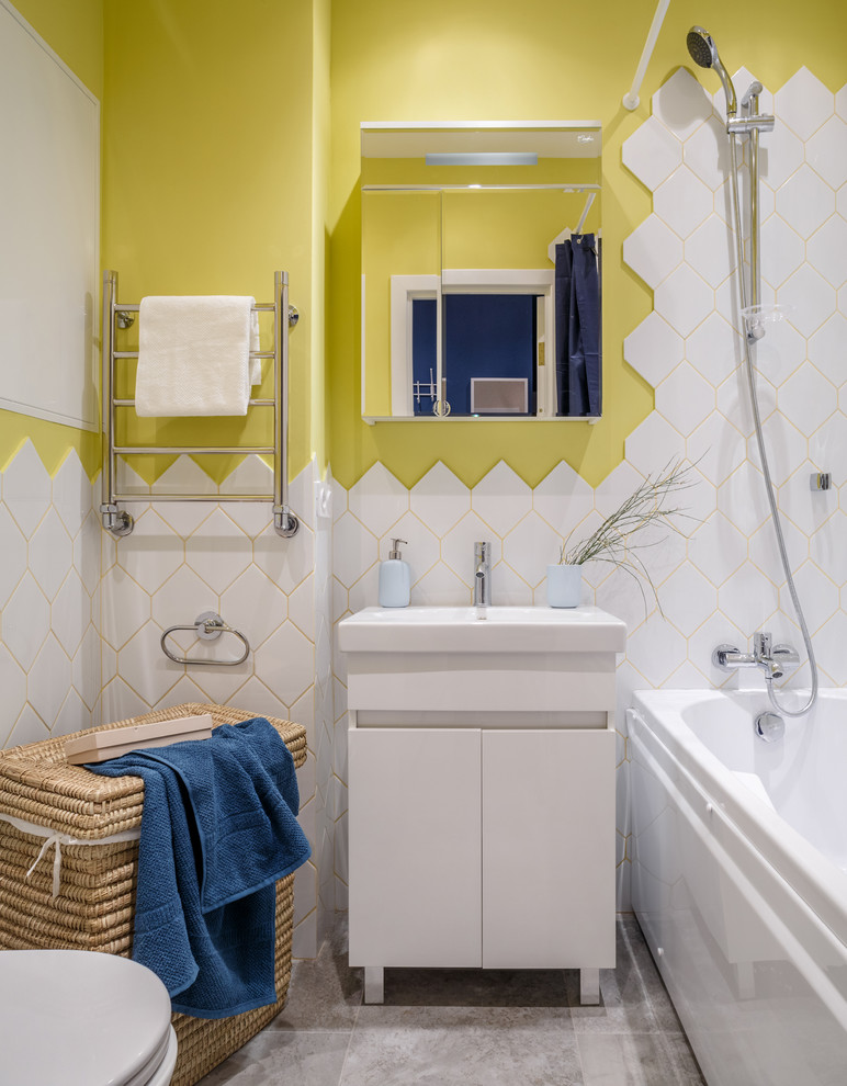 Cette image montre une petite salle de bain principale design avec un placard à porte plane, des portes de placard blanches, une baignoire en alcôve, un combiné douche/baignoire, un carrelage blanc, un mur jaune, un lavabo intégré, un sol gris et une cabine de douche avec un rideau.