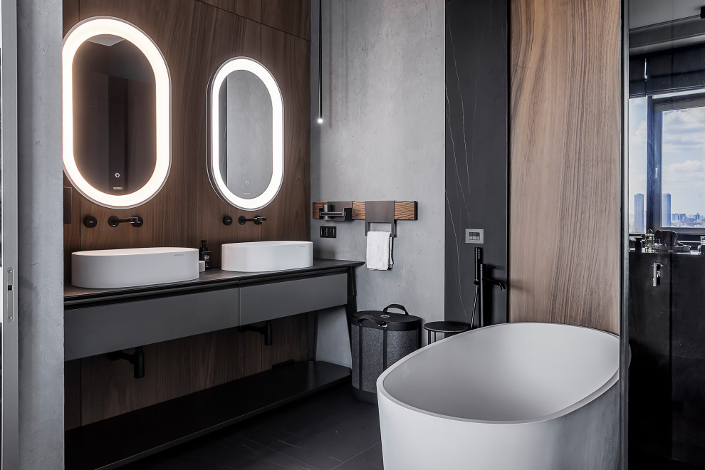 Design ideas for a contemporary ensuite bathroom in Saint Petersburg with flat-panel cabinets, grey cabinets, a freestanding bath, grey walls, a vessel sink, black floors, grey worktops, double sinks and a freestanding vanity unit.