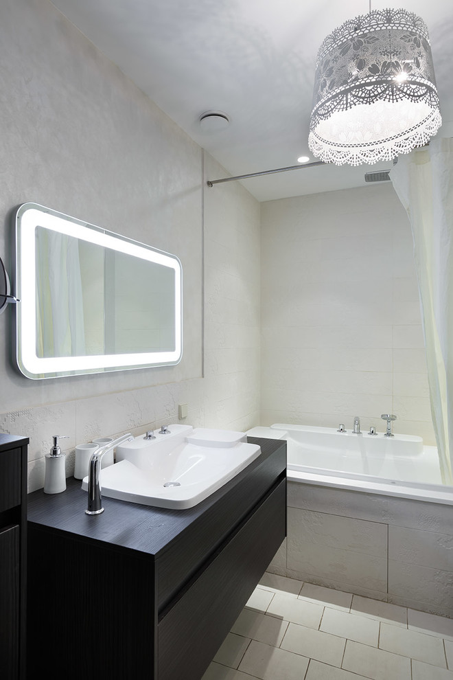 На фото: главная ванная комната в современном стиле с плоскими фасадами, черными фасадами, ванной в нише, серыми стенами, накладной раковиной и зеркалом с подсветкой