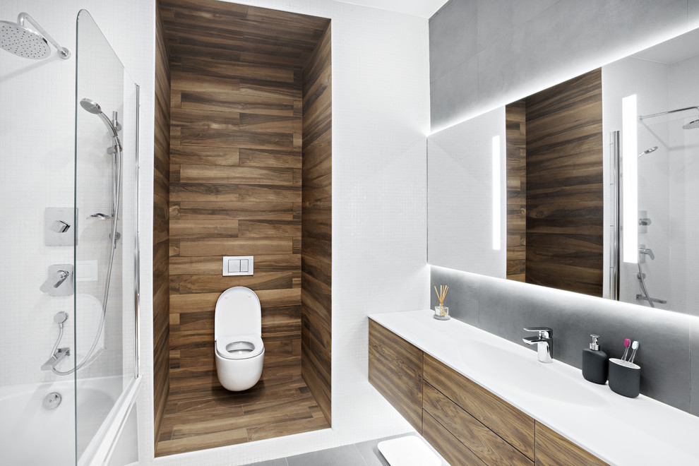 Réalisation d'une salle de bain principale nordique en bois brun avec un placard à porte plane, une baignoire en alcôve, un combiné douche/baignoire, WC suspendus, un carrelage blanc, un lavabo intégré, un sol gris, mosaïque et aucune cabine.