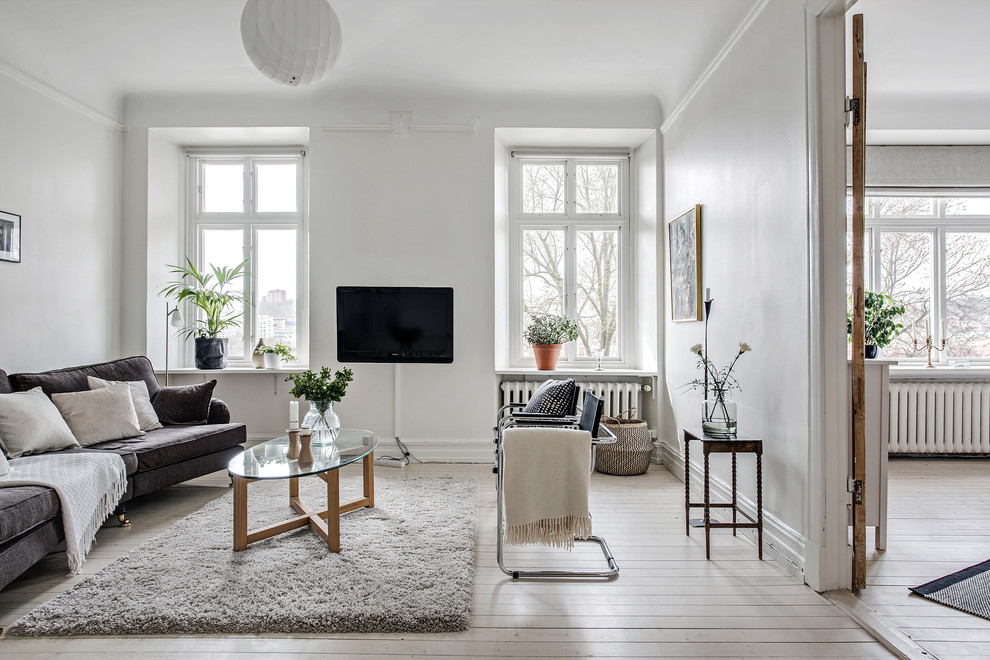 Modelo de salón cerrado nórdico grande sin chimenea con paredes blancas, televisor colgado en la pared, suelo blanco y suelo de madera clara