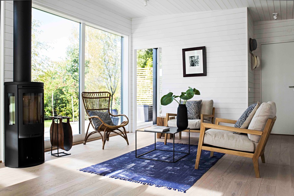 Foto de salón abierto escandinavo de tamaño medio con paredes blancas, suelo de madera clara, estufa de leña y marco de chimenea de metal