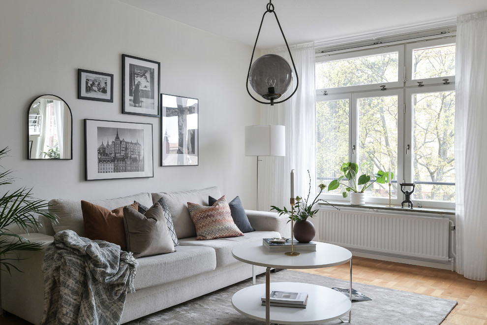 Пример оригинального дизайна: гостиная комната в скандинавском стиле с белыми стенами и светлым паркетным полом