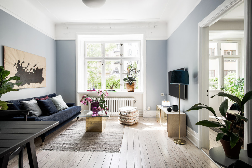 Foto på ett mellanstort minimalistiskt allrum med öppen planlösning, med blå väggar, ljust trägolv och en väggmonterad TV