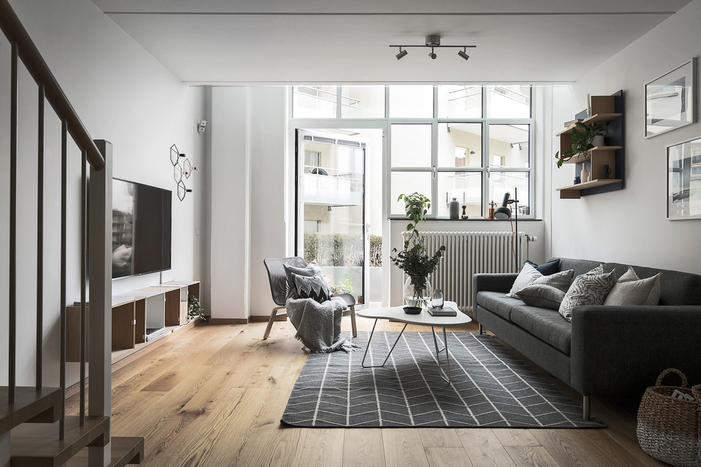 Nordisk inredning av ett vardagsrum, med vita väggar, en väggmonterad TV och brunt golv