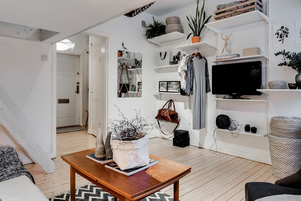 Inredning av ett minimalistiskt litet separat vardagsrum, med vita väggar, ljust trägolv och en fristående TV