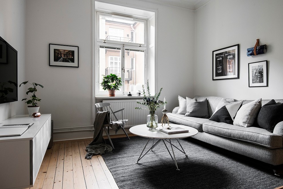 Skandinavisk inredning av ett vardagsrum, med vita väggar, mellanmörkt trägolv, en väggmonterad TV och beiget golv