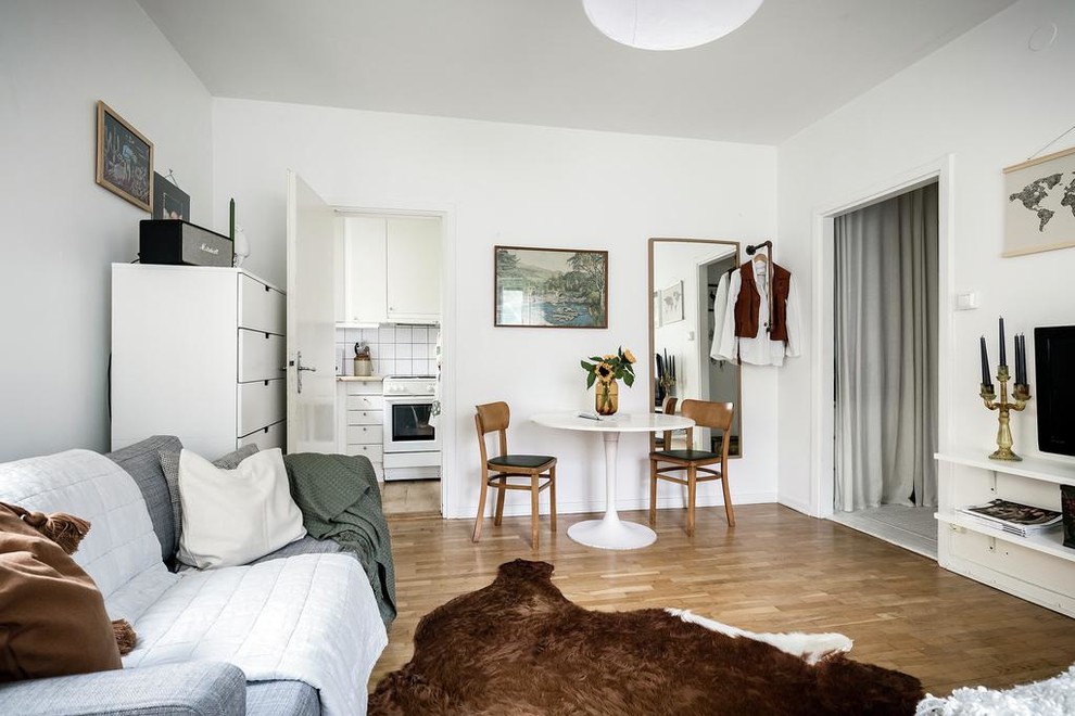 Diseño de salón abierto escandinavo pequeño con paredes blancas, suelo de madera en tonos medios, televisor colgado en la pared y suelo marrón