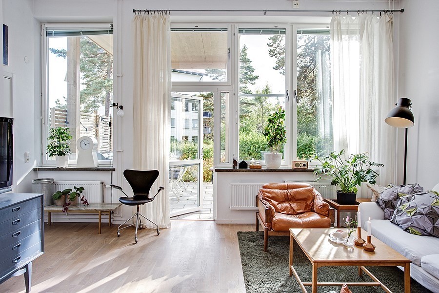 Modelo de salón abierto escandinavo grande con paredes blancas, suelo de madera clara, televisor independiente y suelo marrón