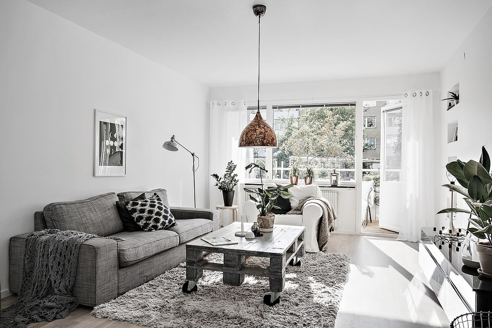 This is an example of a medium sized scandinavian formal open plan living room in Gothenburg with white walls, light hardwood flooring, no tv and feature lighting.