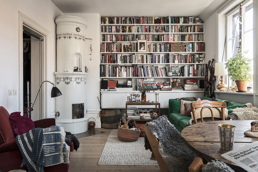 Idee per un piccolo soggiorno boho chic aperto con libreria, pareti bianche, parquet chiaro, stufa a legna e cornice del camino piastrellata