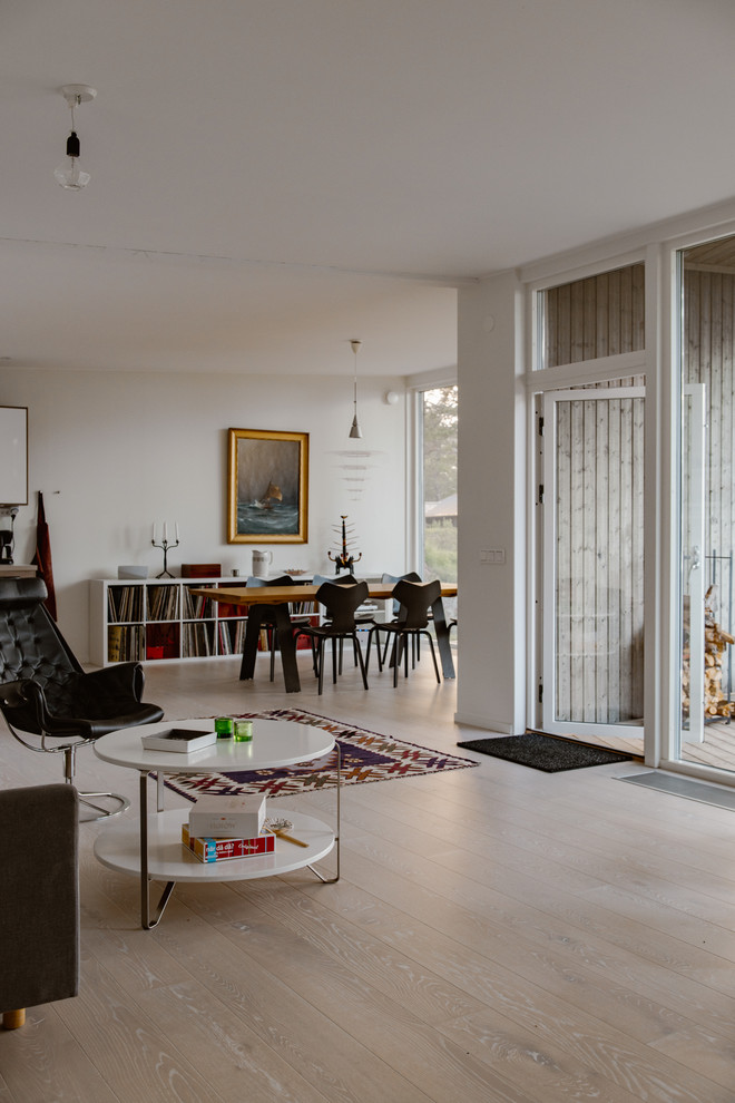 На фото: открытая гостиная комната среднего размера в скандинавском стиле с белыми стенами и полом из ламината с