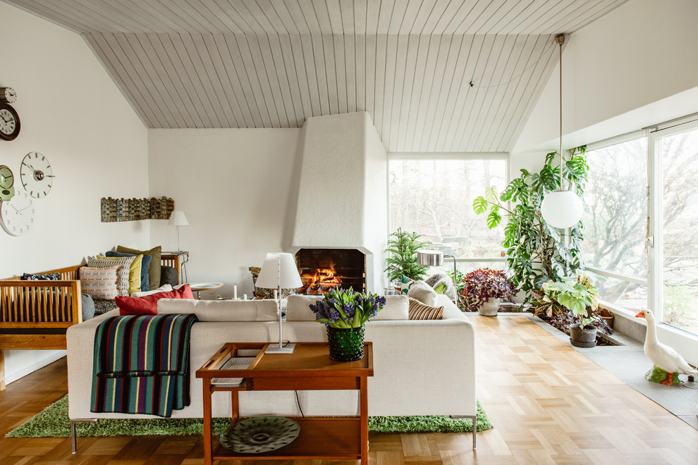 Großes Retro Wohnzimmer mit weißer Wandfarbe, braunem Holzboden, verputzter Kaminumrandung, beigem Boden und Kamin in Stockholm