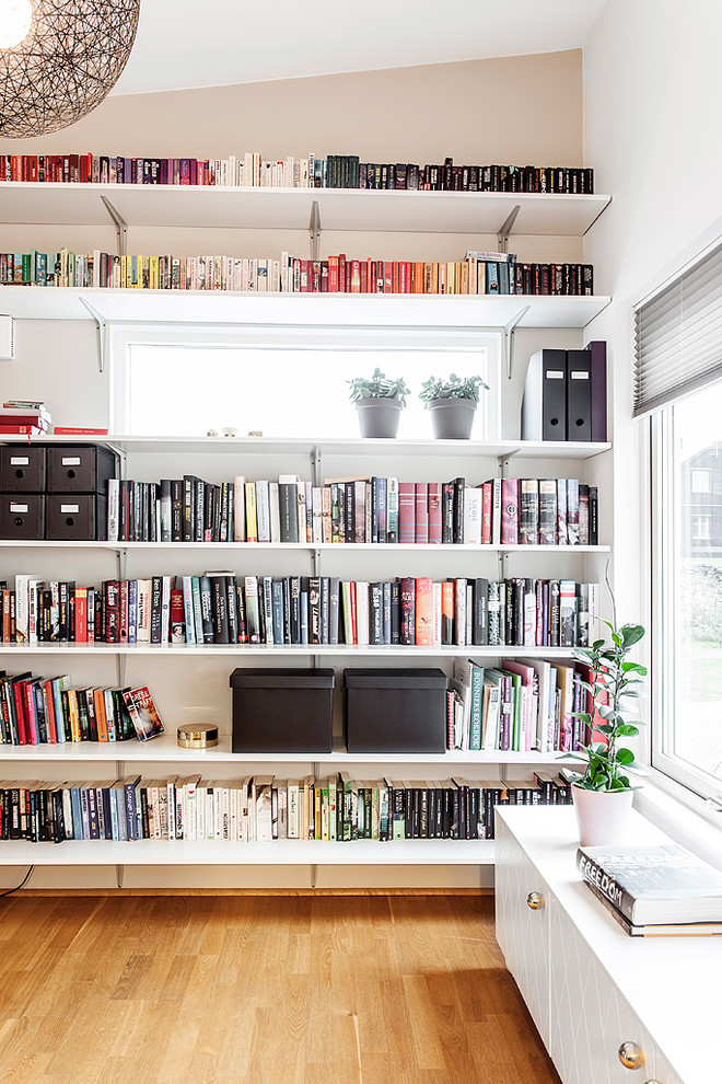 Esempio di un grande soggiorno nordico aperto con libreria, pareti bianche, pavimento in legno massello medio, TV a parete e pavimento nero