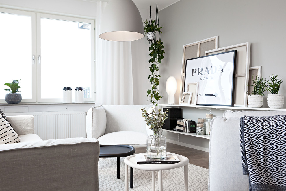 Modelo de salón escandinavo grande sin televisor con paredes blancas, suelo de madera clara y suelo marrón