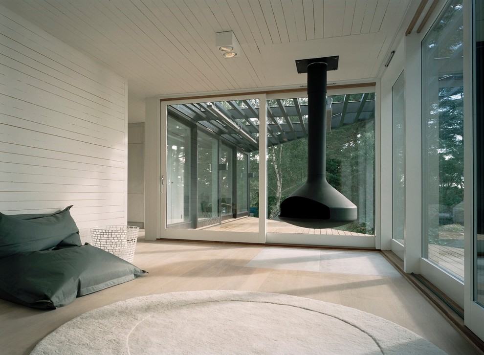 Example of a large danish enclosed light wood floor living room design in Stockholm with white walls and a hanging fireplace