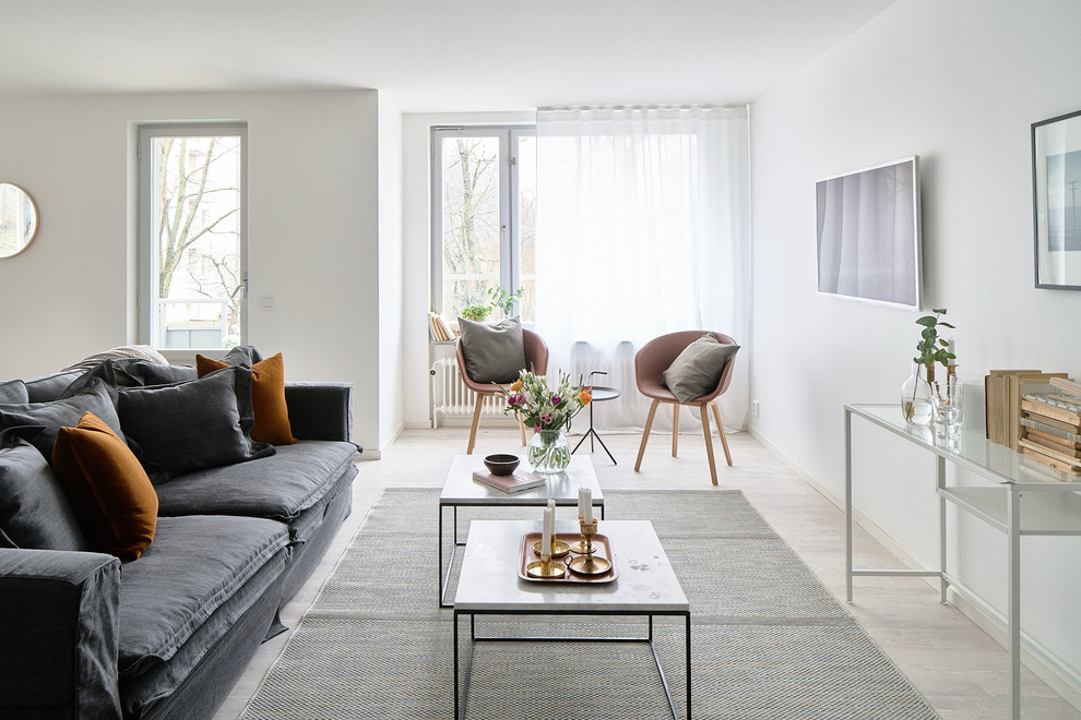 Modelo de salón abierto escandinavo de tamaño medio sin chimenea con paredes blancas, suelo de madera clara y televisor colgado en la pared