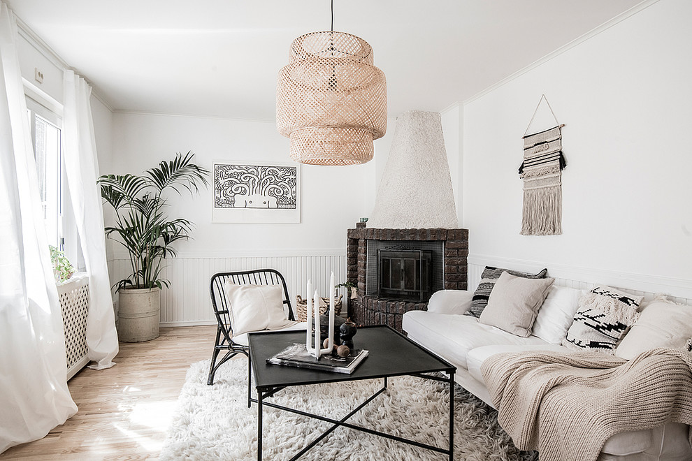 Abgetrenntes, Fernseherloses Skandinavisches Wohnzimmer mit weißer Wandfarbe, hellem Holzboden, Eckkamin, Kaminumrandung aus Backstein und beigem Boden in Stockholm