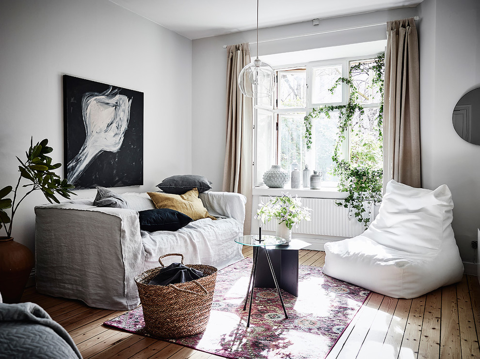 На фото: изолированная гостиная комната в скандинавском стиле с белыми стенами и светлым паркетным полом без камина с