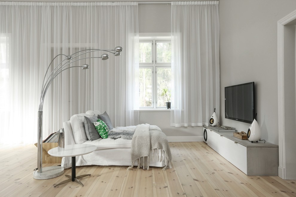 This is an example of a large scandinavian living room with white walls, light hardwood flooring and a wall mounted tv.