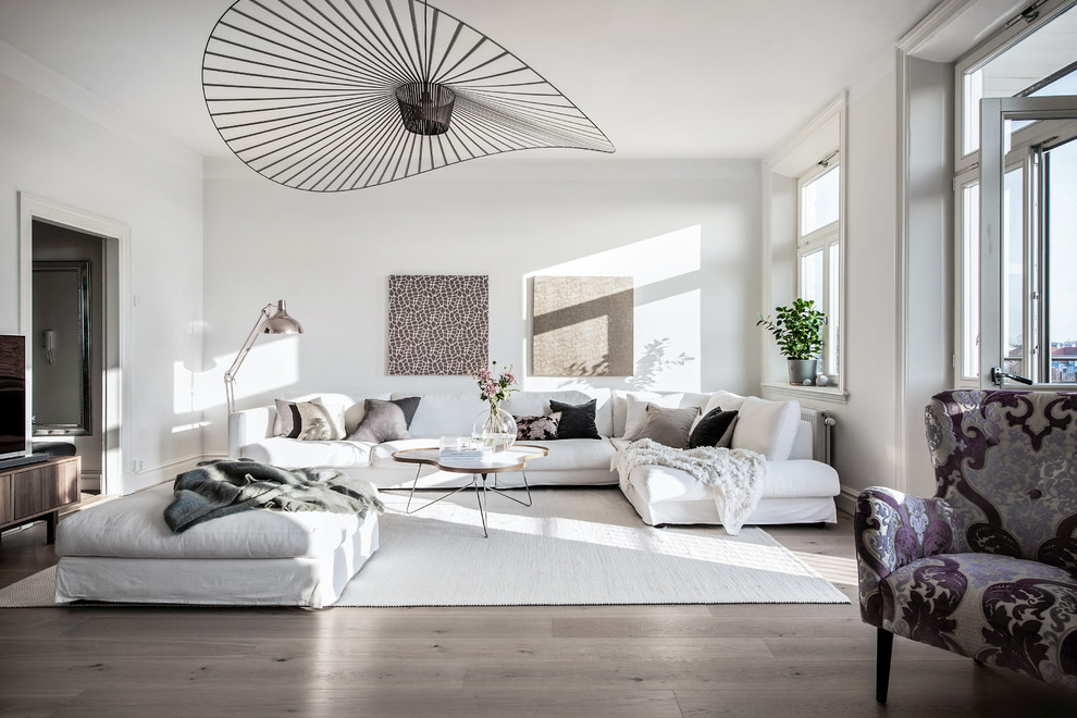 Nordisk inredning av ett vardagsrum, med vita väggar, ljust trägolv, en fristående TV och beiget golv