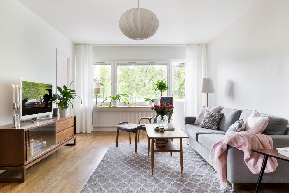 Example of a mid-sized danish formal and enclosed medium tone wood floor living room design in Stockholm with white walls and a tv stand