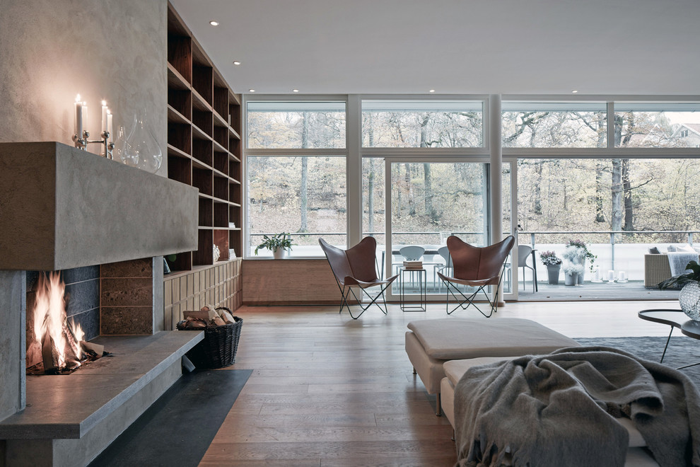 Cette image montre un grand salon design avec un sol en bois brun, une cheminée standard et un téléviseur fixé au mur.