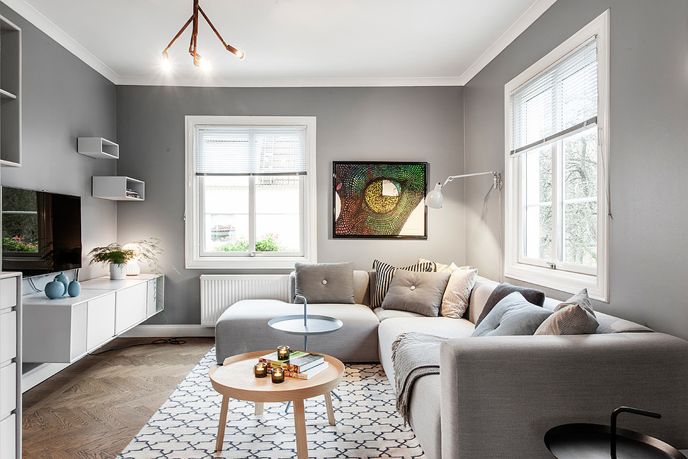 This is an example of a medium sized scandi enclosed living room in Gothenburg with grey walls, light hardwood flooring, a wall mounted tv and beige floors.
