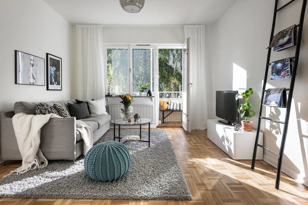 This is an example of a medium sized scandinavian grey and teal enclosed living room in Stockholm with white walls, medium hardwood flooring, a freestanding tv and brown floors.