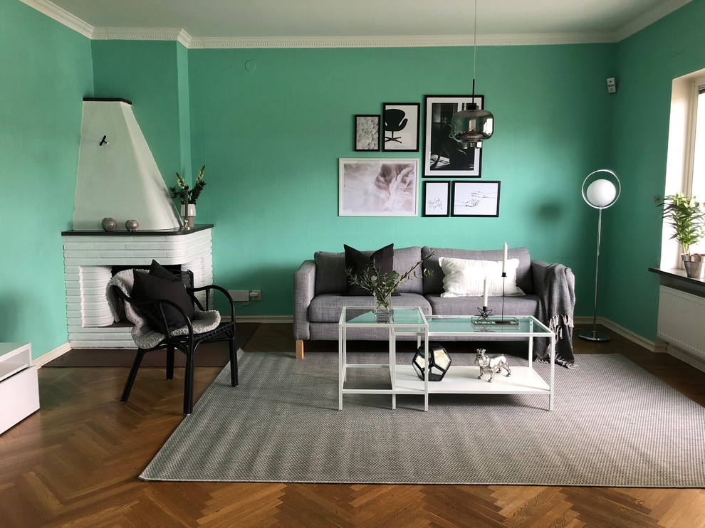 Bild på ett stort funkis separat vardagsrum, med gröna väggar, mellanmörkt trägolv, en öppen hörnspis, brunt golv och en spiselkrans i tegelsten