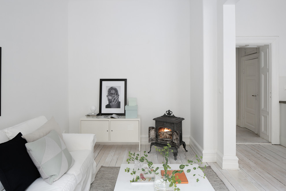 Immagine di un piccolo soggiorno scandinavo con pareti bianche, pavimento in legno verniciato, stufa a legna e nessuna TV