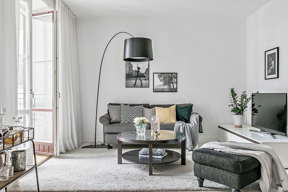 Skandinavisk inredning av ett mellanstort vardagsrum, med vita väggar, en fristående TV och grått golv